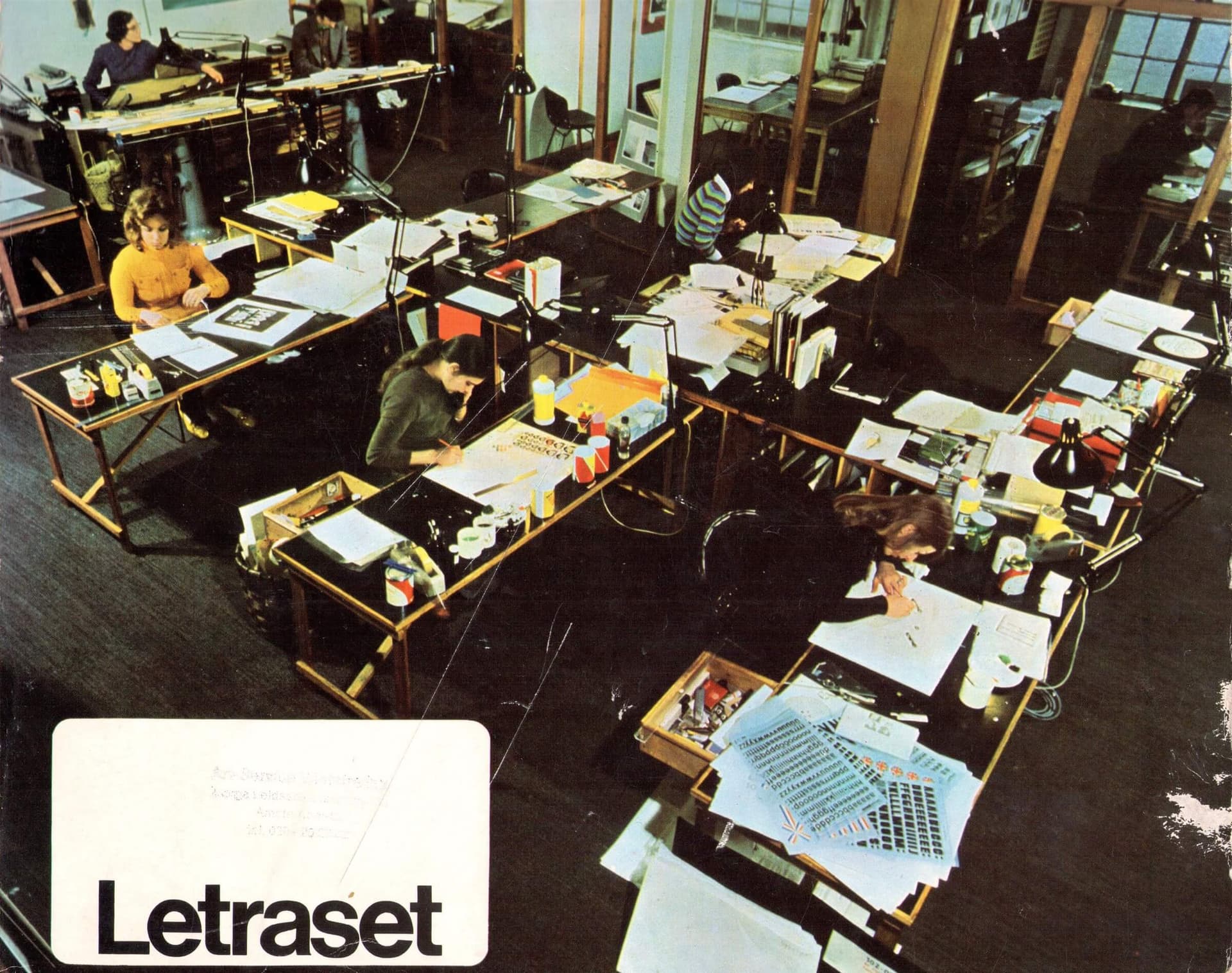 A graphic design agency or the layout department of a magazine on the cover of a Letraset catalogue, with an overview of rub-down lettering in a range of fonts and self-adhesive foils in a range of colours, patterns, symbols and signs, c.1975. 