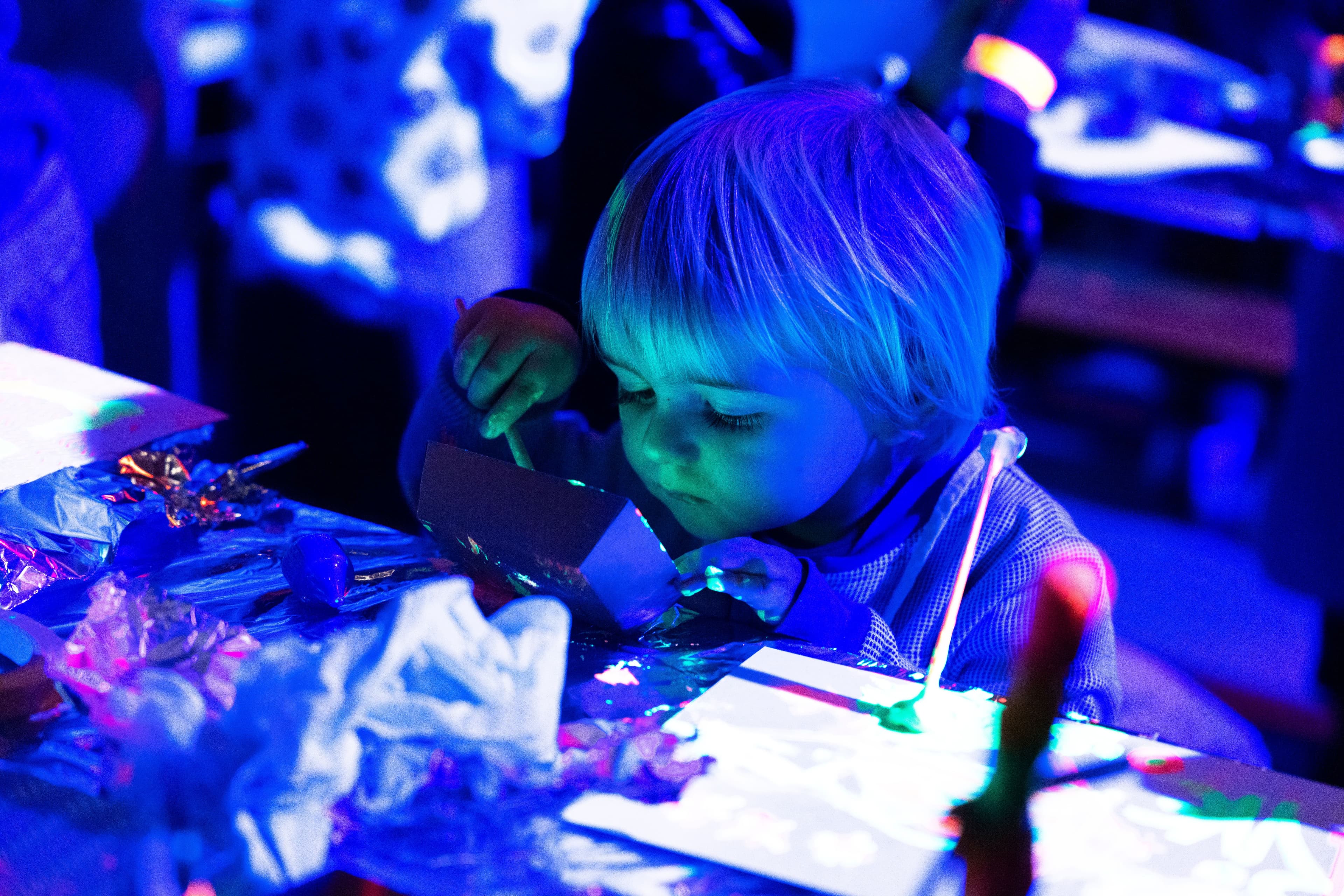 Een peuter knutselt aandachtig aan een lichtbak met groen licht in een blauw verlichte ruimte