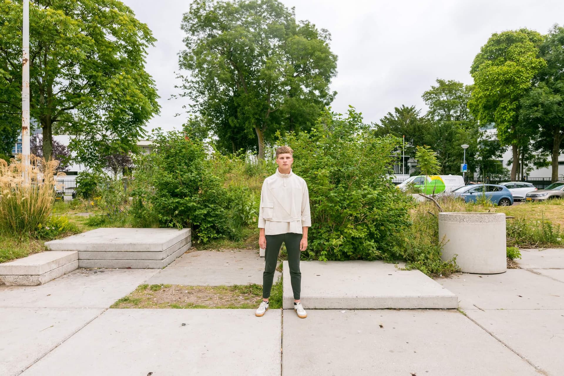 A person in green trousers and white jacket is standing in the garden.