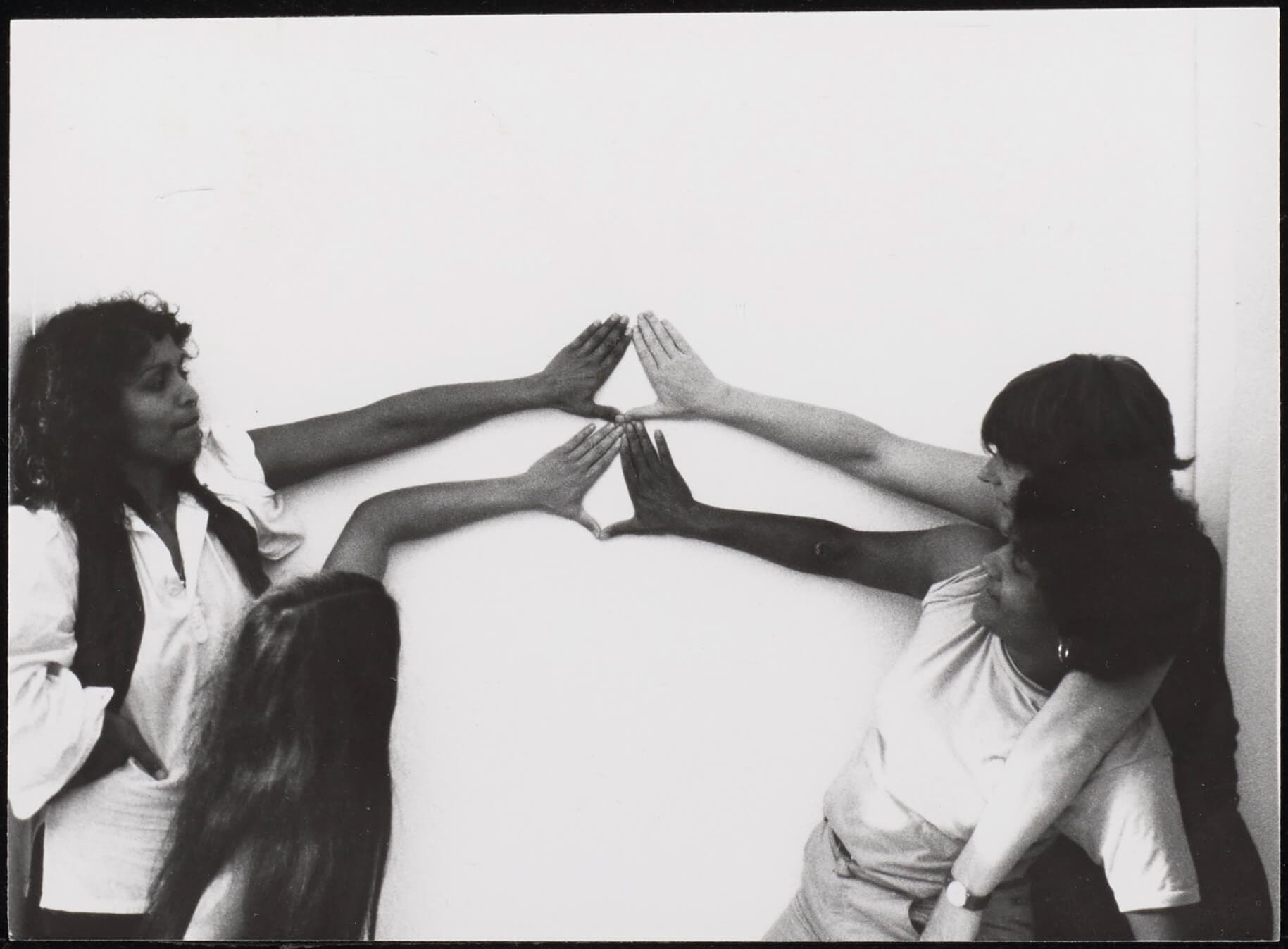 Four women forming triangles, or the Yoni sign, with their hands against a white wall, counter clockwise from bottom right: Tania Leon, Lida van den Broek, Ananda Spies, Margrethe Rumeser, year: 198?, photo: Gon Buurman. Source: Collection IAV-A…