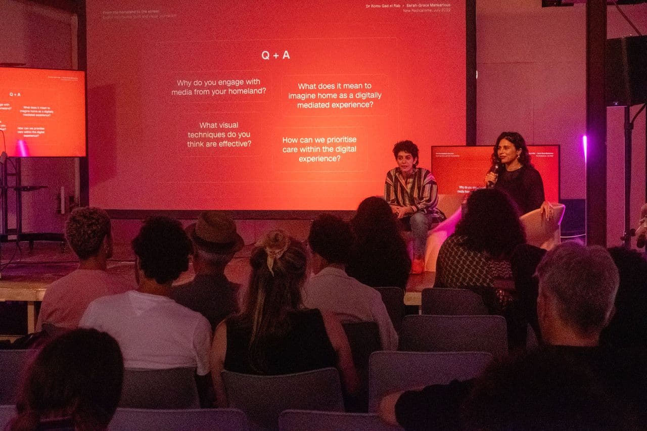 Two people on stage answering question with a red background and a crowd