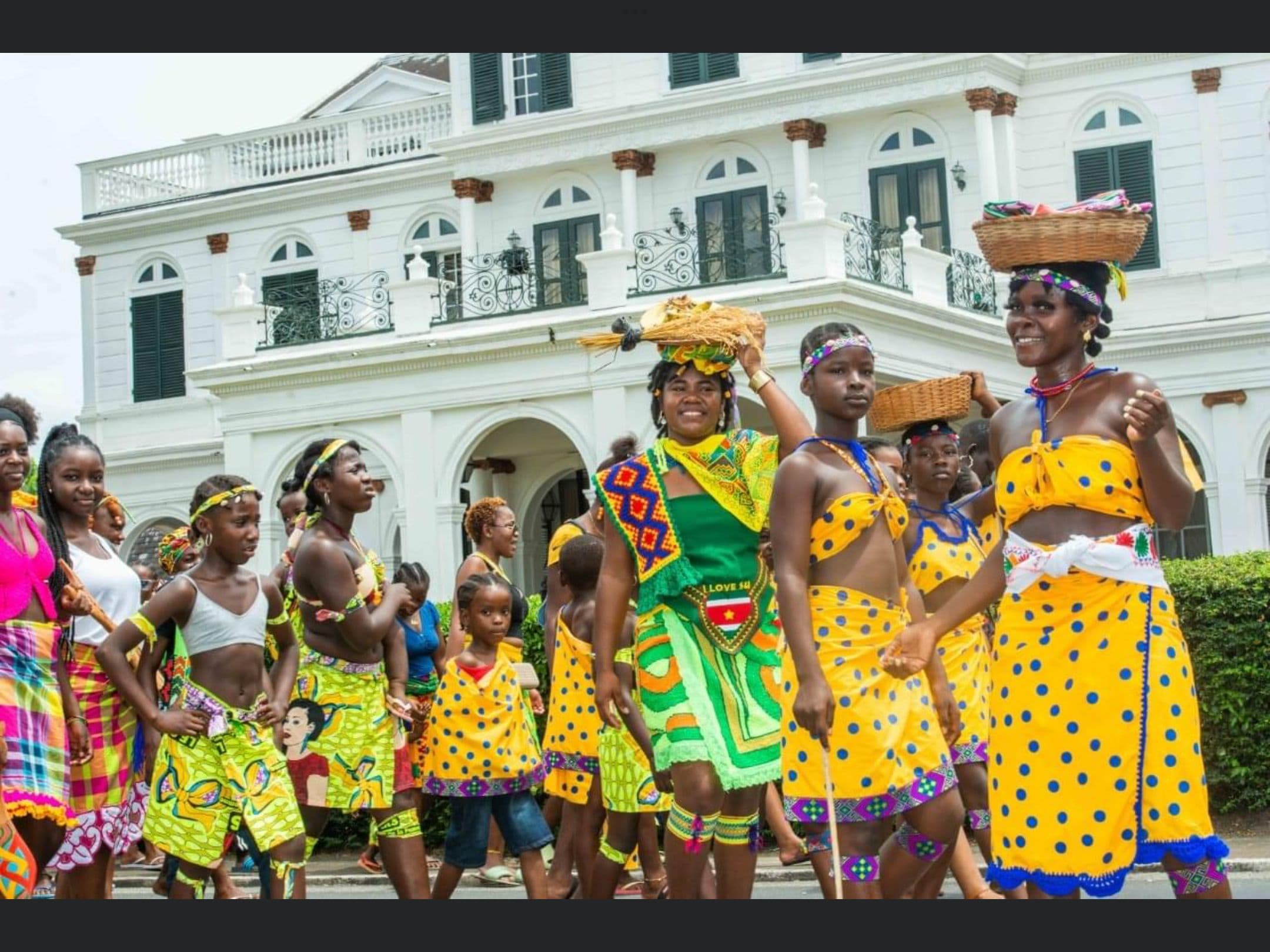A group of Indigenous Surinamese and Marron women and girls in traditional clothing, parading down the street