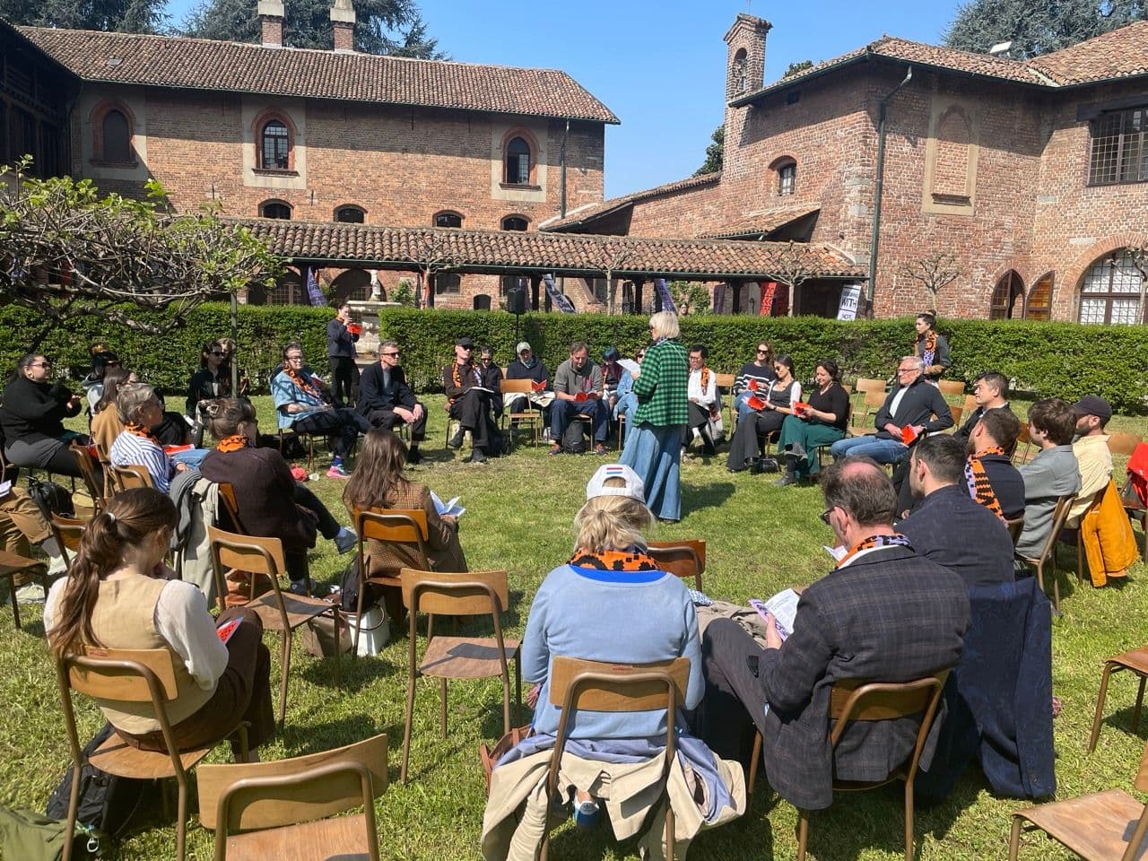 Mensen wonen het Milaanse CIVICITY event bij. Ze zitten in een cirkel op stoelen in een groene tuin.
