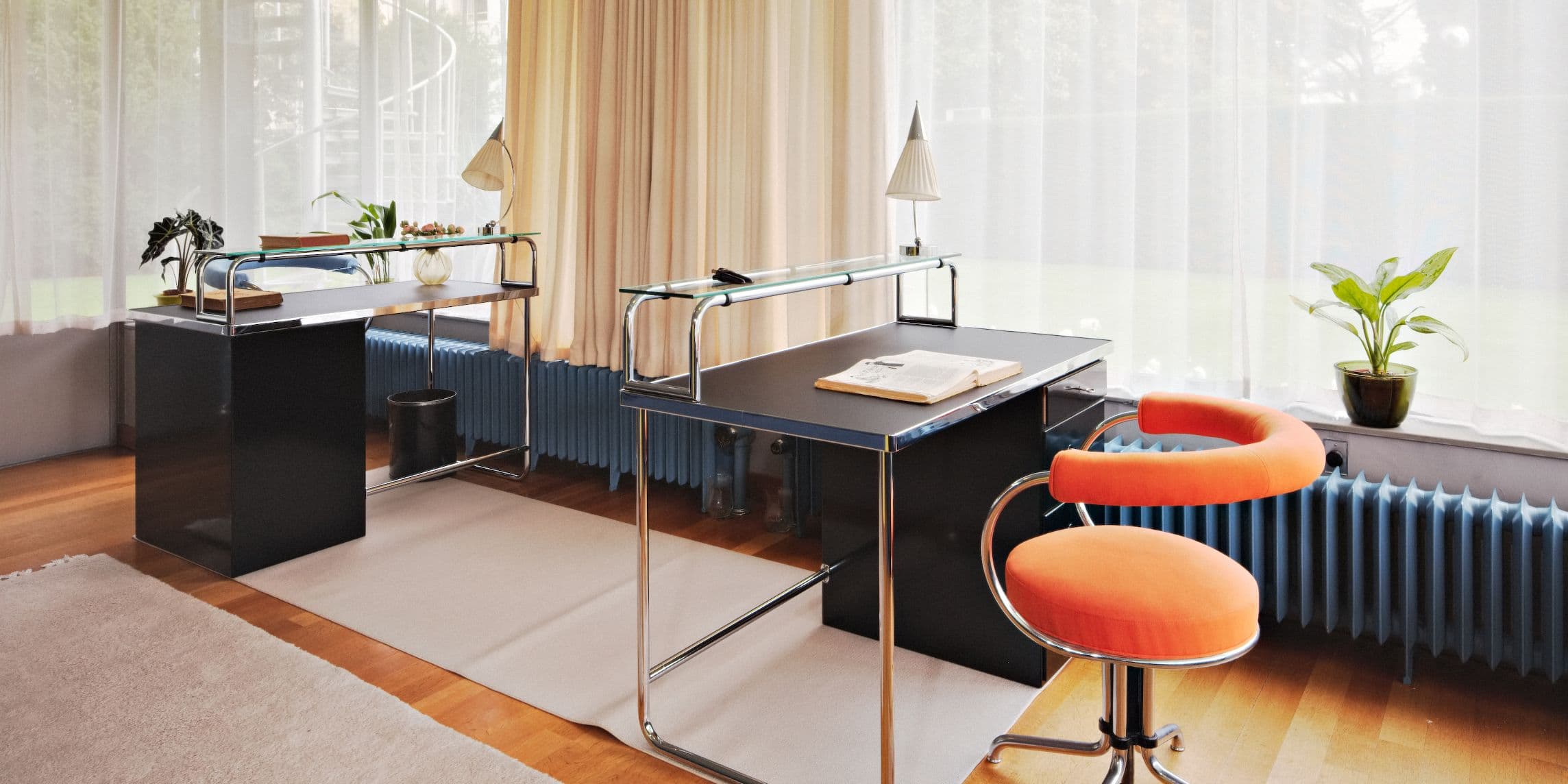 Een moderne kantoorruimte met glazen bureaus, oranje stoelen, planten en zacht natuurlijk licht door doorschijnende gordijnen.