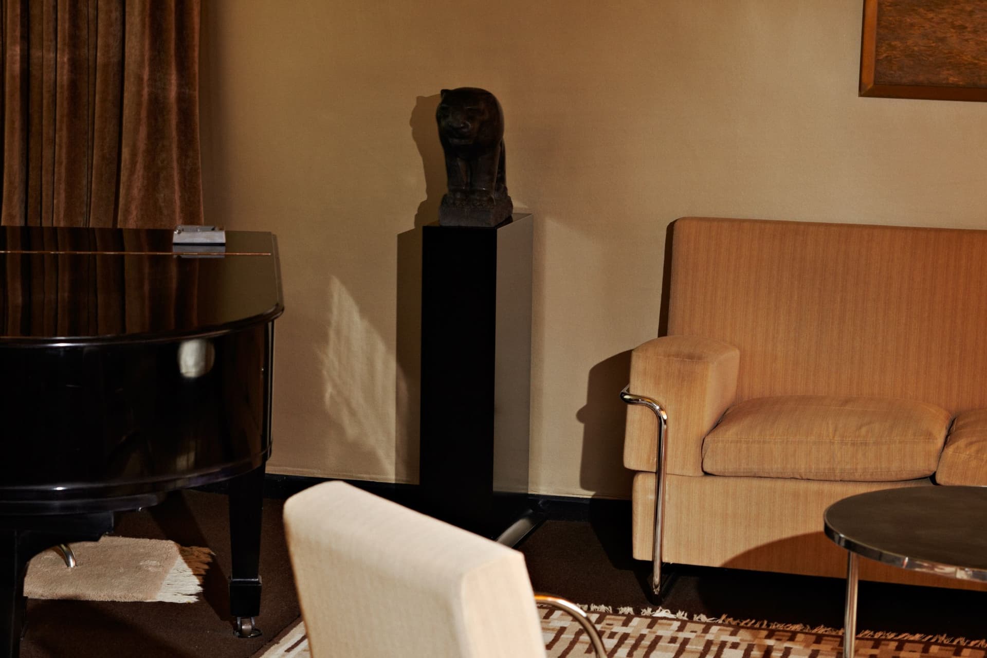 Dimly lit living room with piano, sofa and the (touchable) statue by John Raedecker on a pedestal. Photo by Johannes Schwartz.