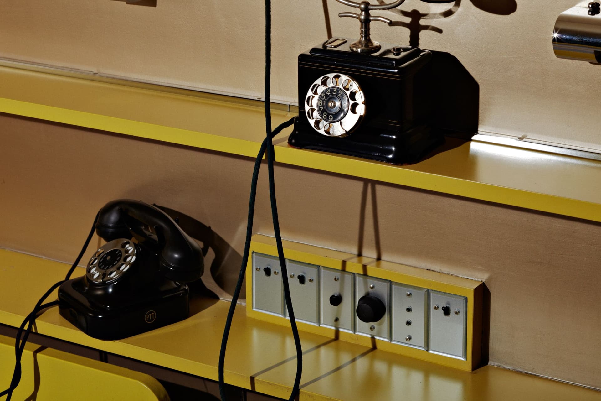 Twee zwarte, bakelieten telefoontoestellen op de plankjes boven het bed in de ouderslaapkamer. 