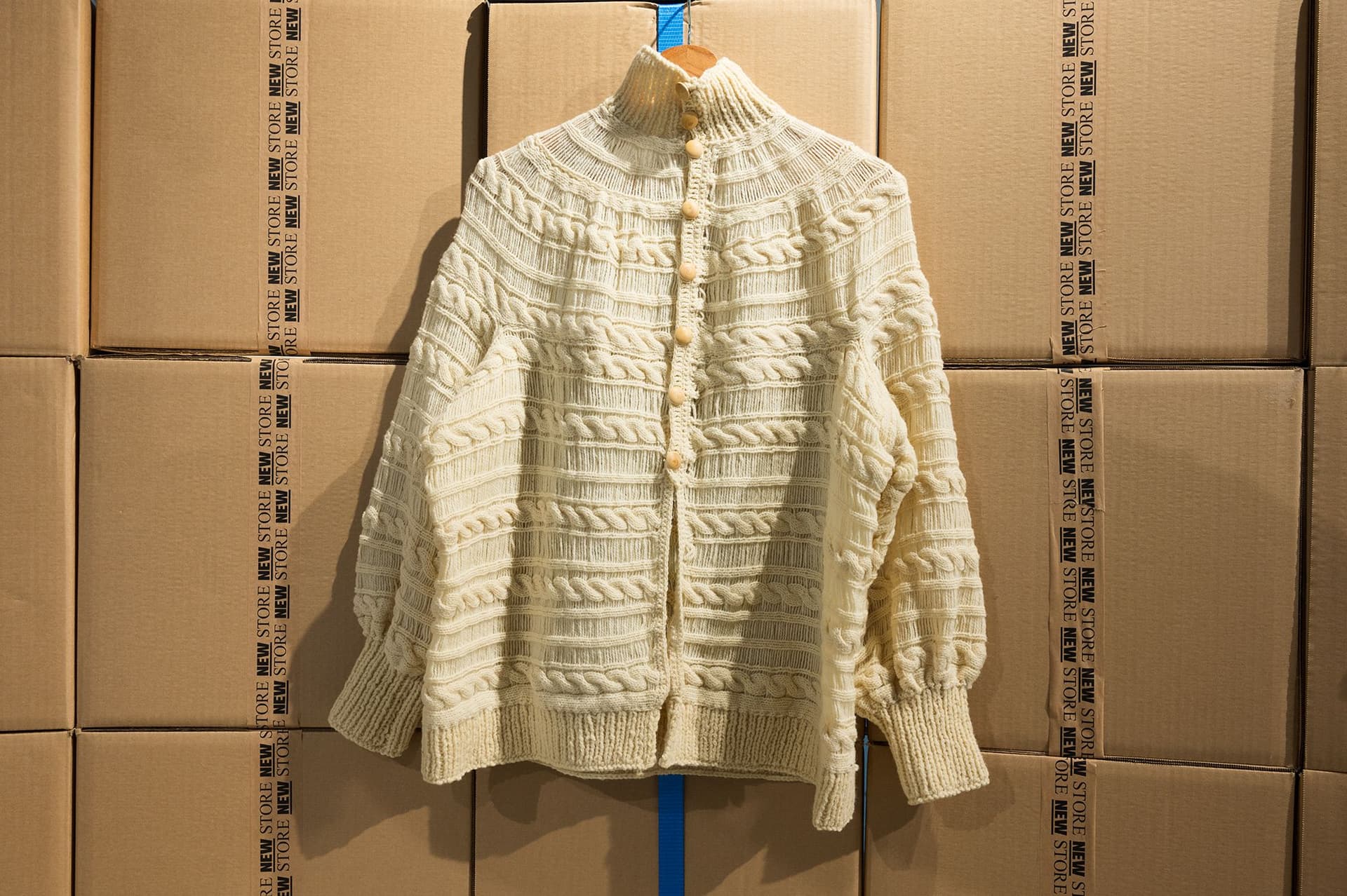 A yellow, wool sweater displayed on a clothing hanger against a backdrop of carton boxes in the New Store. Photo: Petra van der Ree