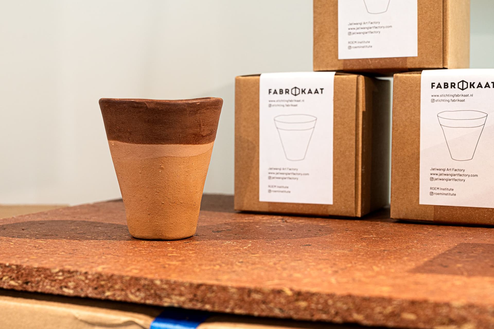 The cup made out of clay and beeswax displayed on a table with packaging from Fabrikaat in the background. Photo: Petra van der Ree