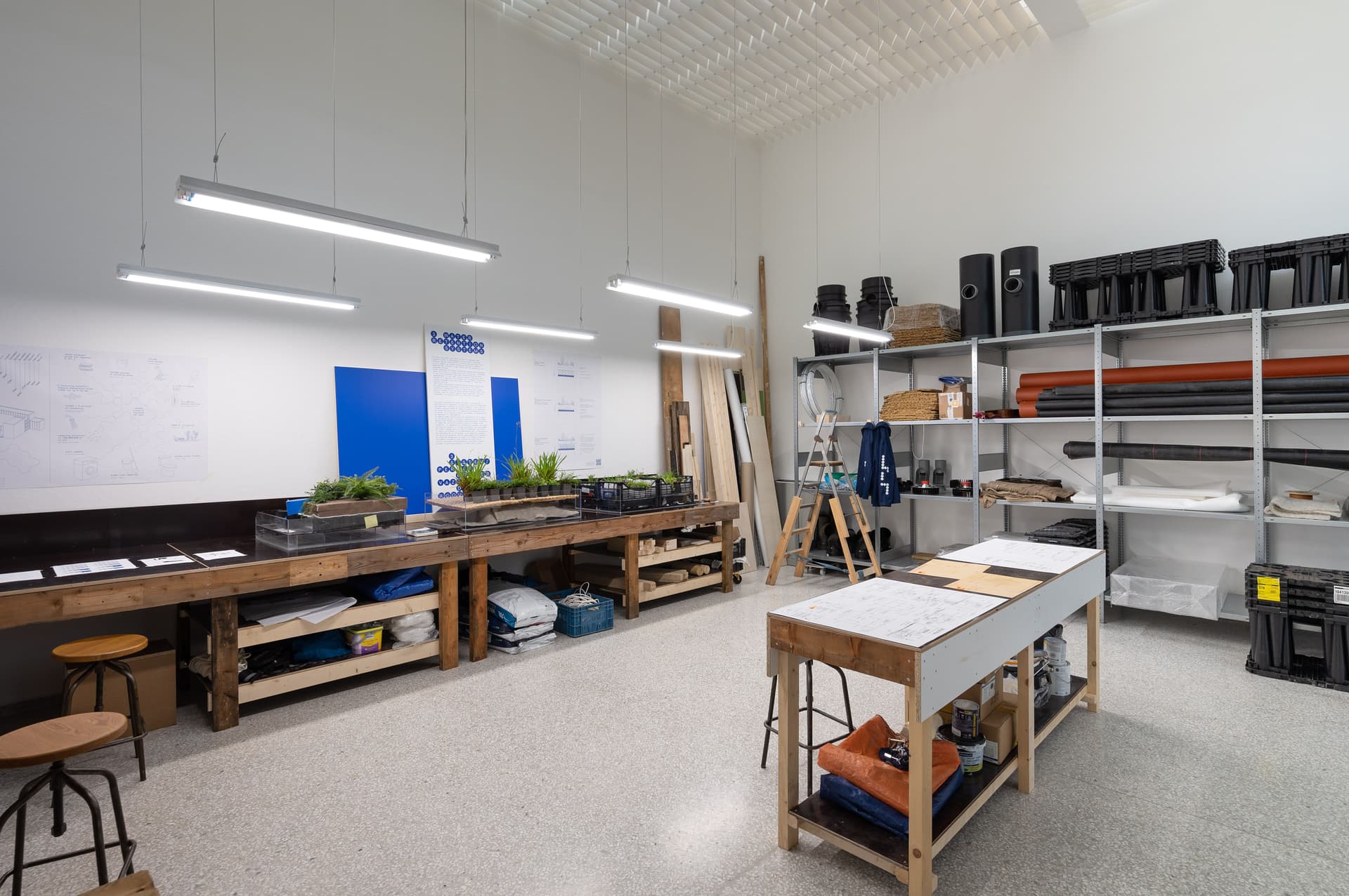 Photo of exhibition space, set up like a working station. With long desks, shelving units and TL lights.