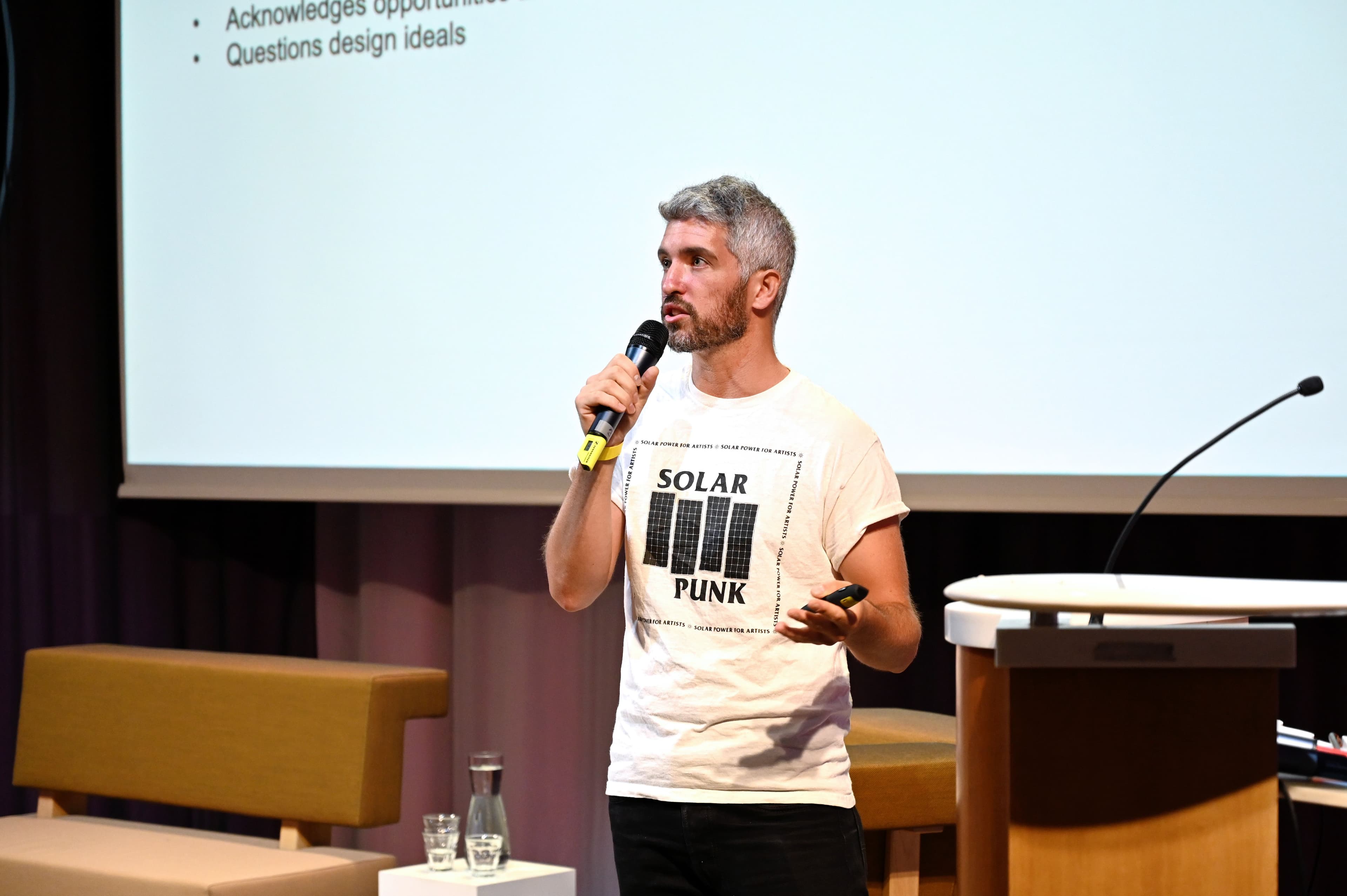 Alex Nathanson presenteert met een microfoon voor een wit scherm