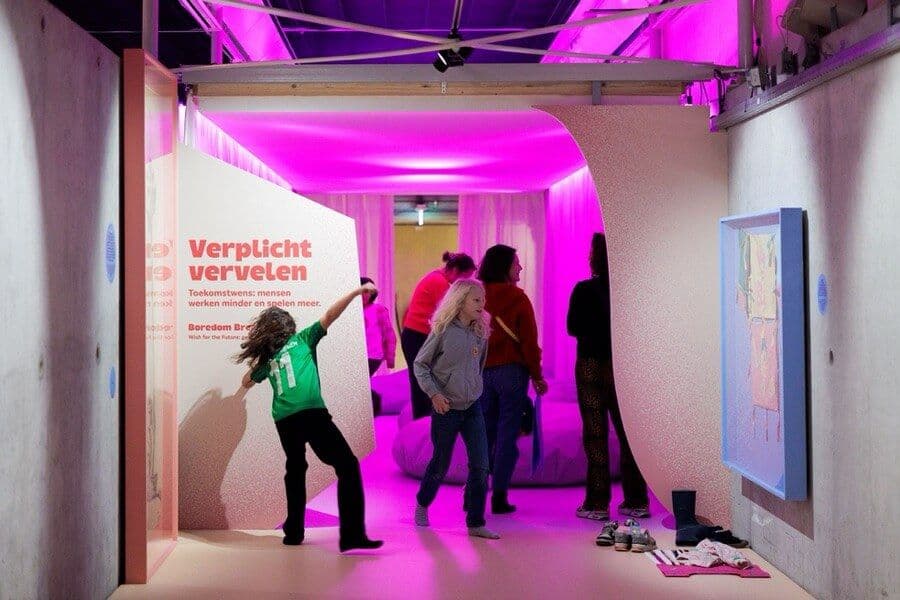 The exhibition space of the Future Makers exhibition showing pink light shining through the hall with childen running around in the foreground. Photo: Aad Hoogendoorn