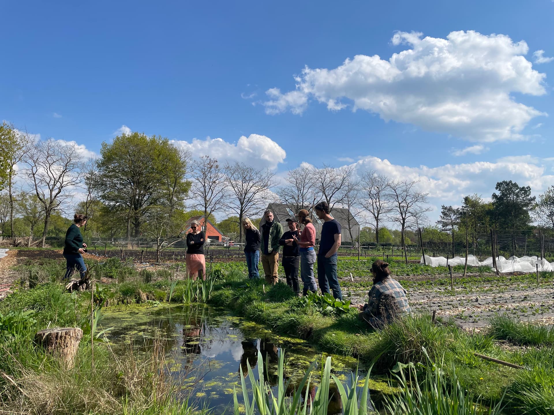 Bezoekers van de Bodemzicht Boerderij staan in een grasveld bij een plas.