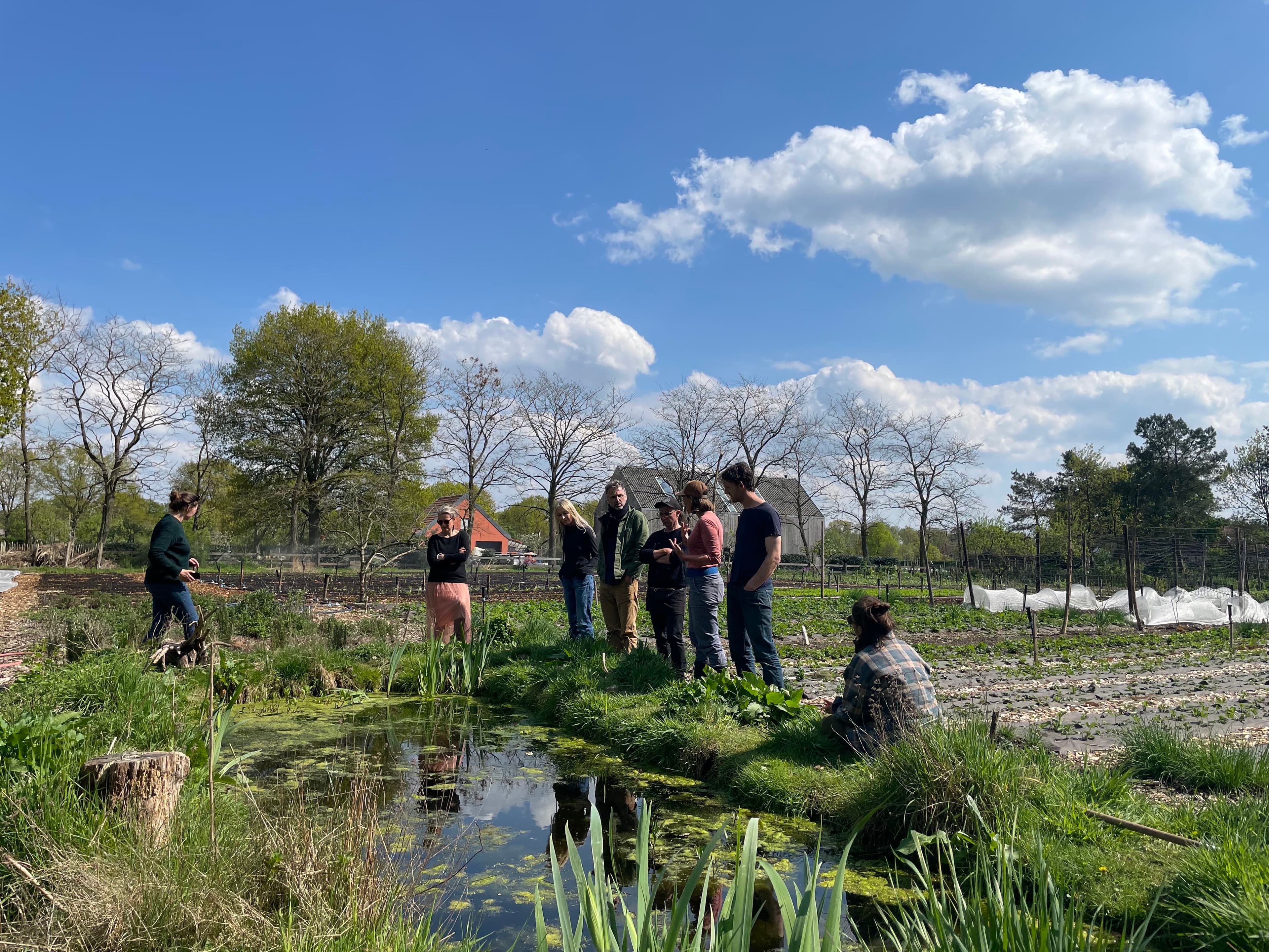 Bezoekers van de Bodemzicht Boerderij staan in een grasveld bij een plas.