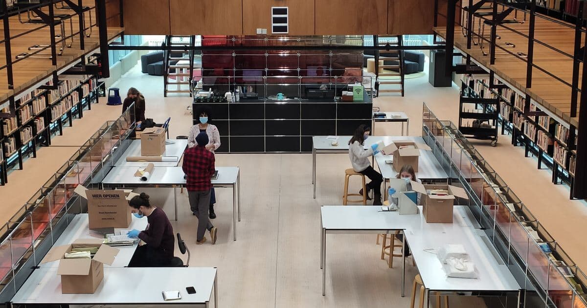 The research room at Het Nieuwe Instituut. Wooden floors and paneling in various shades of light brown, with black vertical supports and bookcases.