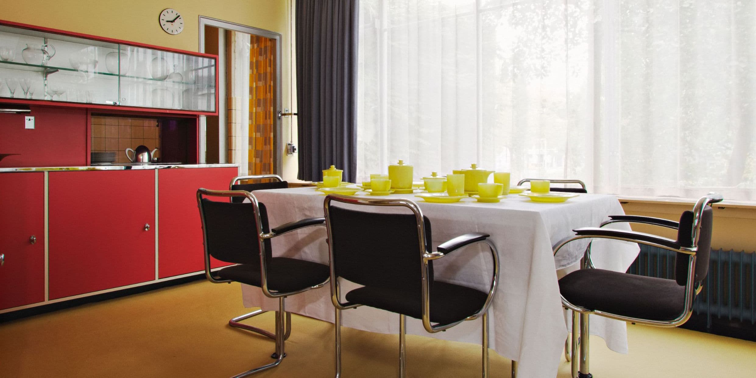 Interior of Sonneveld House, with red cabinets, a dining table with black chairs and yellow dinnerware.
