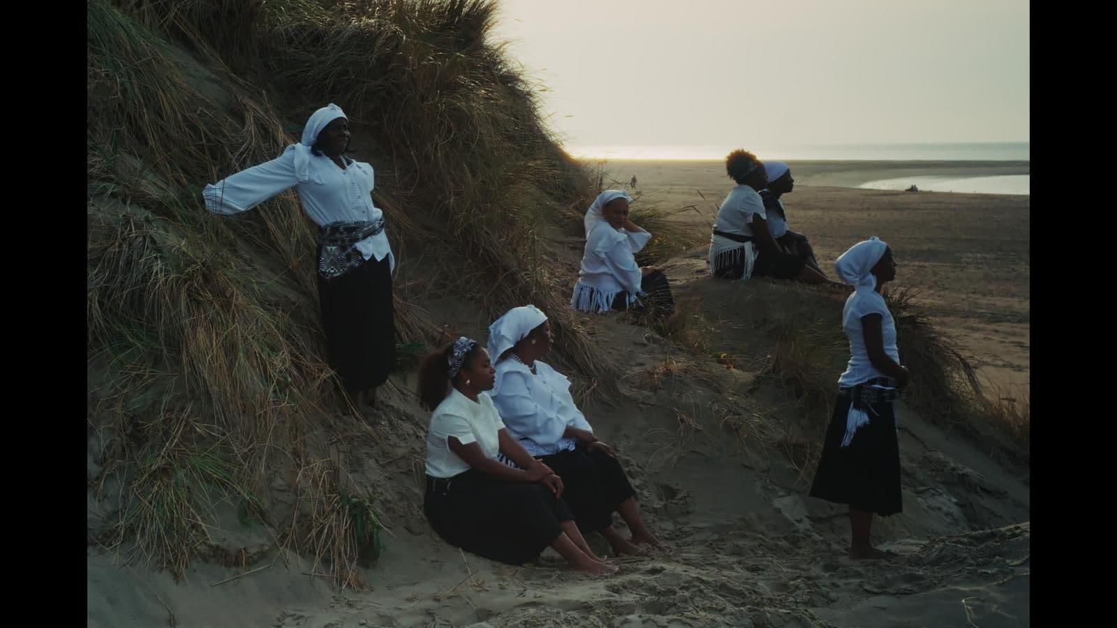 Mensen zitten op een duin met de zee zichtbaar op de achtergrond. Beeld: Janilda Bartolomeu