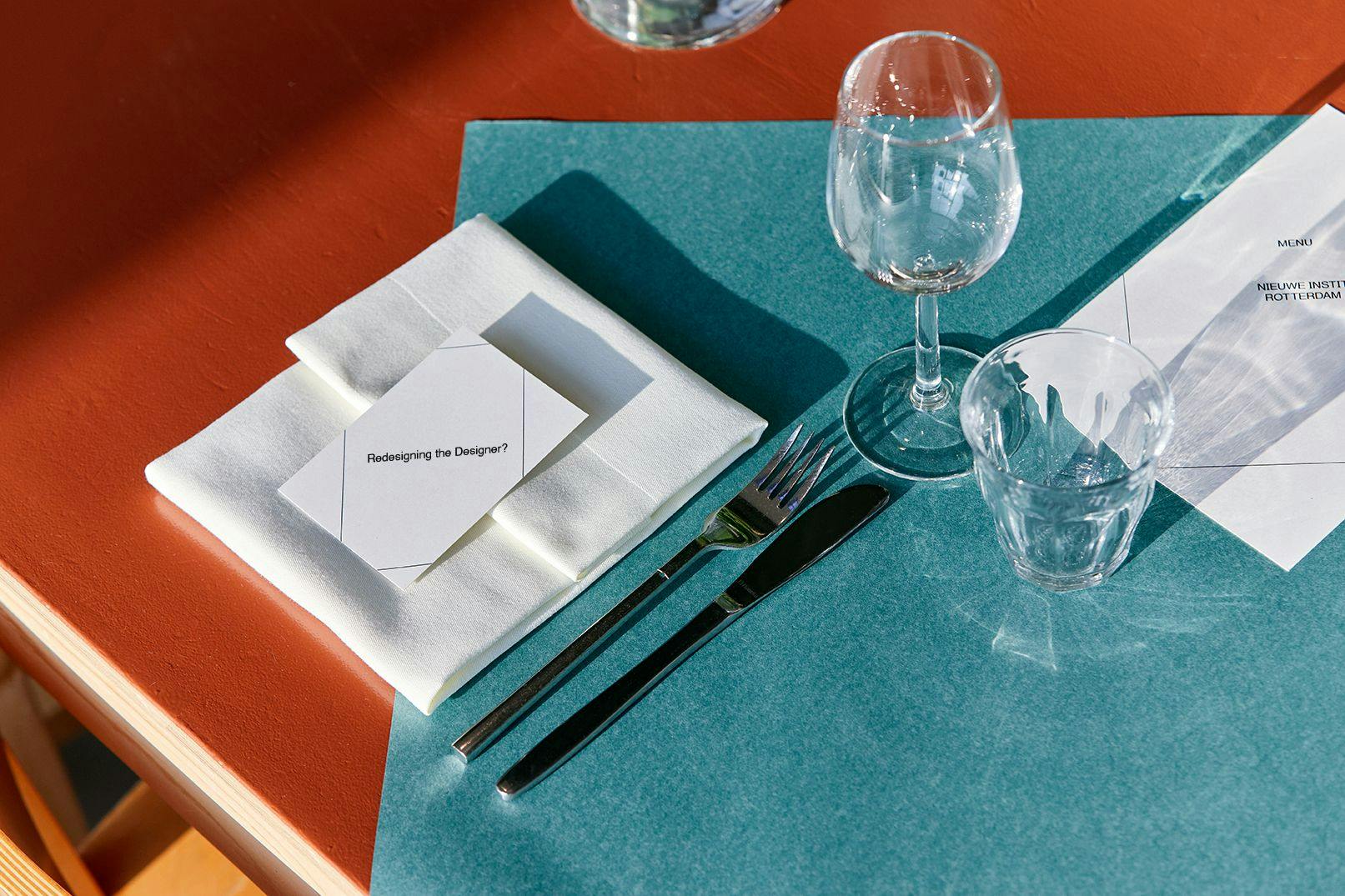 A set table with cards, napkin, silverware, wine glass and glass cup.