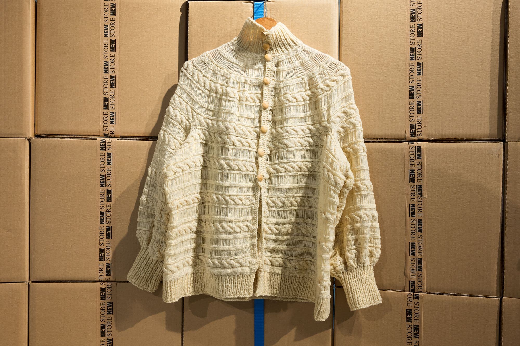 A yellow, wool sweater displayed on a clothing hanger against a backdrop of carton boxes in the New Store. Photo: Petra van der Ree