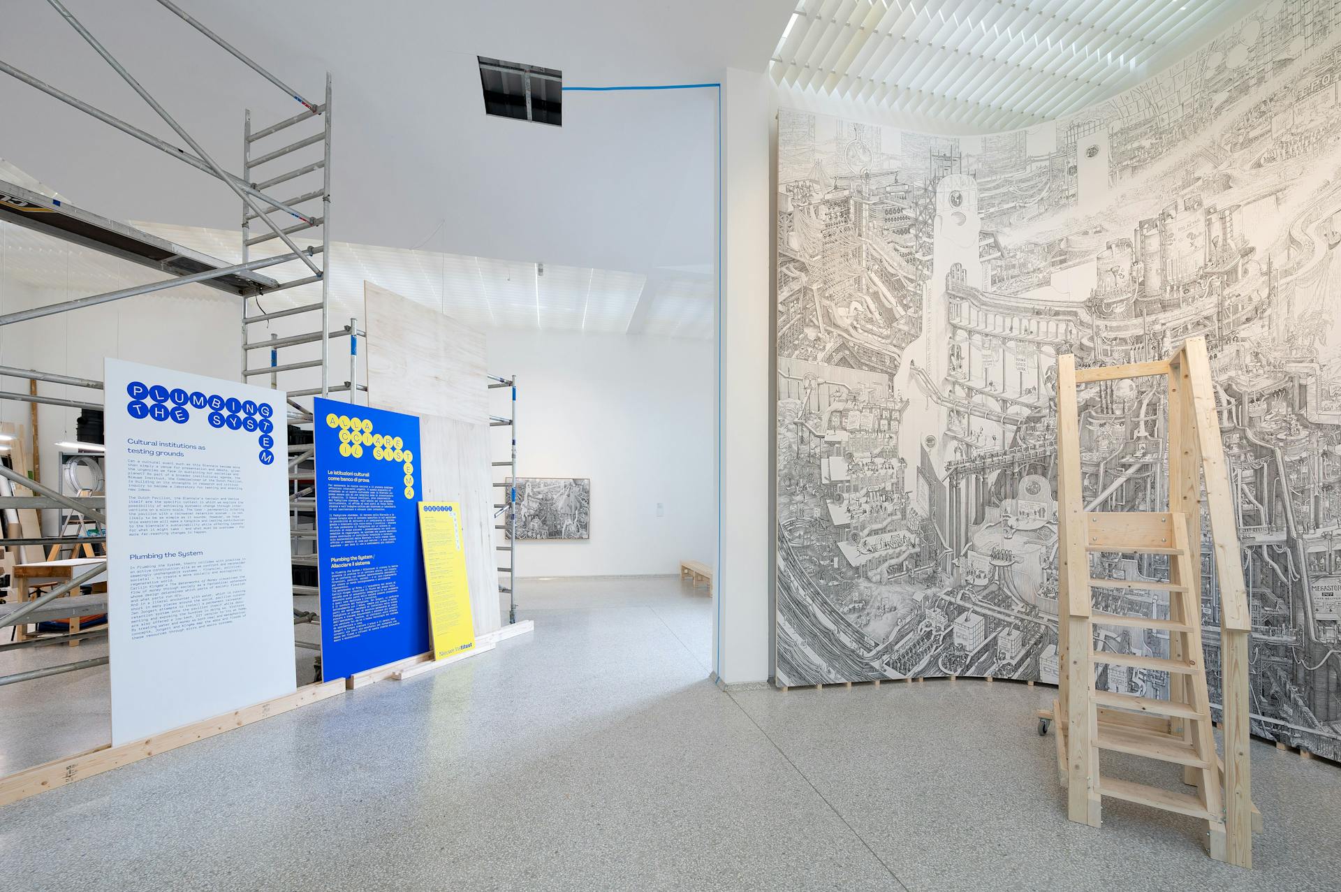 Image of an exhibition space. On the left a scaffold with room texts in graphic design, on the right a detailed drawing as high as the wall, with a staircase for closer viewing.