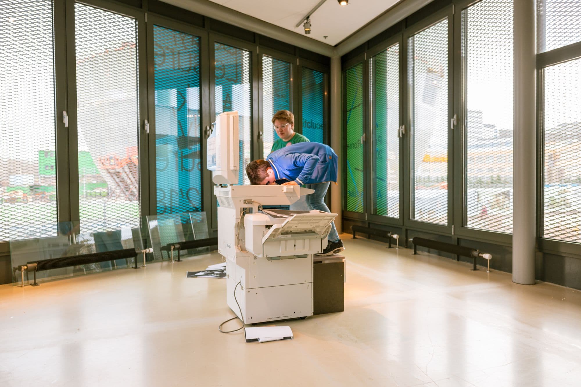 Two children are standing near a printer, trying to copy their faces.